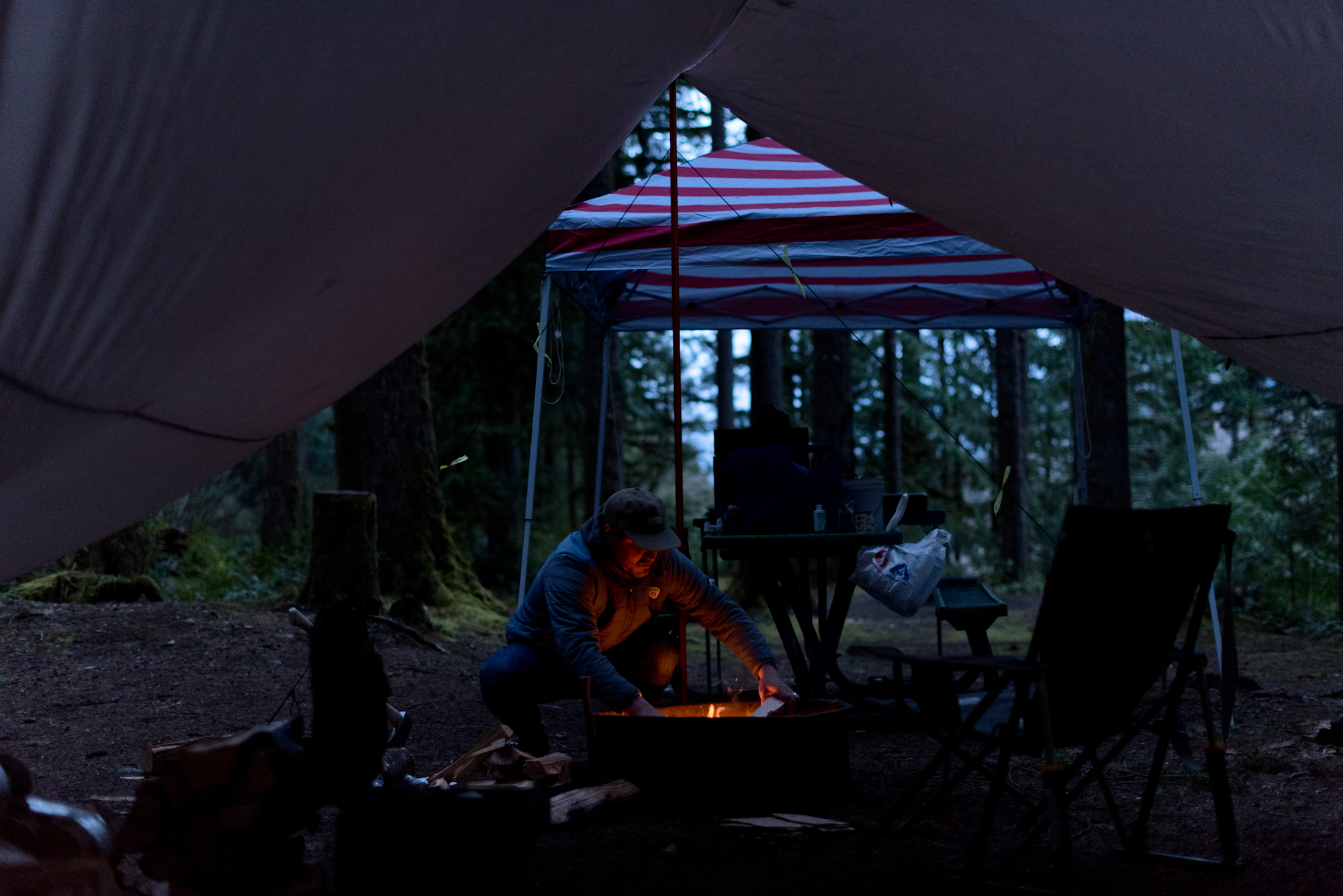 A low light photograph of a man tending to a campfire.